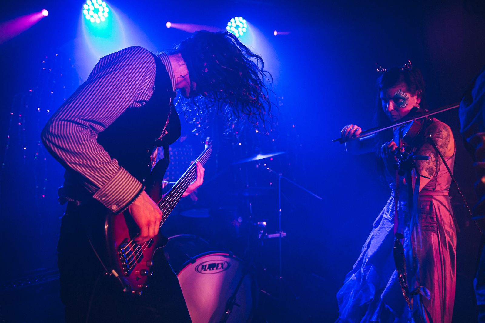 Bassist and violinist leaning into their instruments under deep blue and pink stage lights.